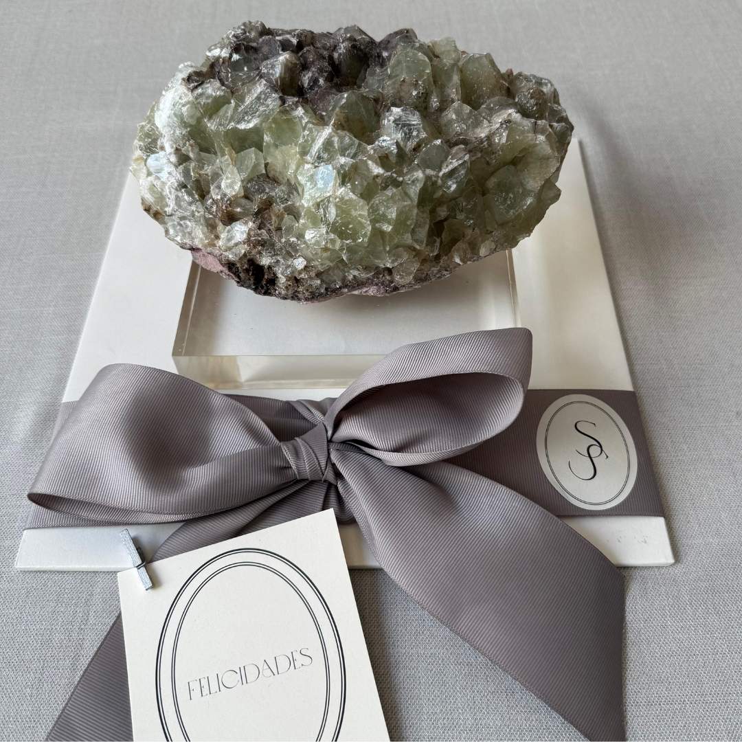 CALCITA VERDE EN BASE DE ACRÍLICO, piedra natural en tono verde translúcido con brillo sutil, montada sobre base acrílica transparente, diseño de SSIENTO que resalta su elegancia moderna como elemento decorativo único para el hogar. Esta pieza puede variar en forma, tamaño y tonos.